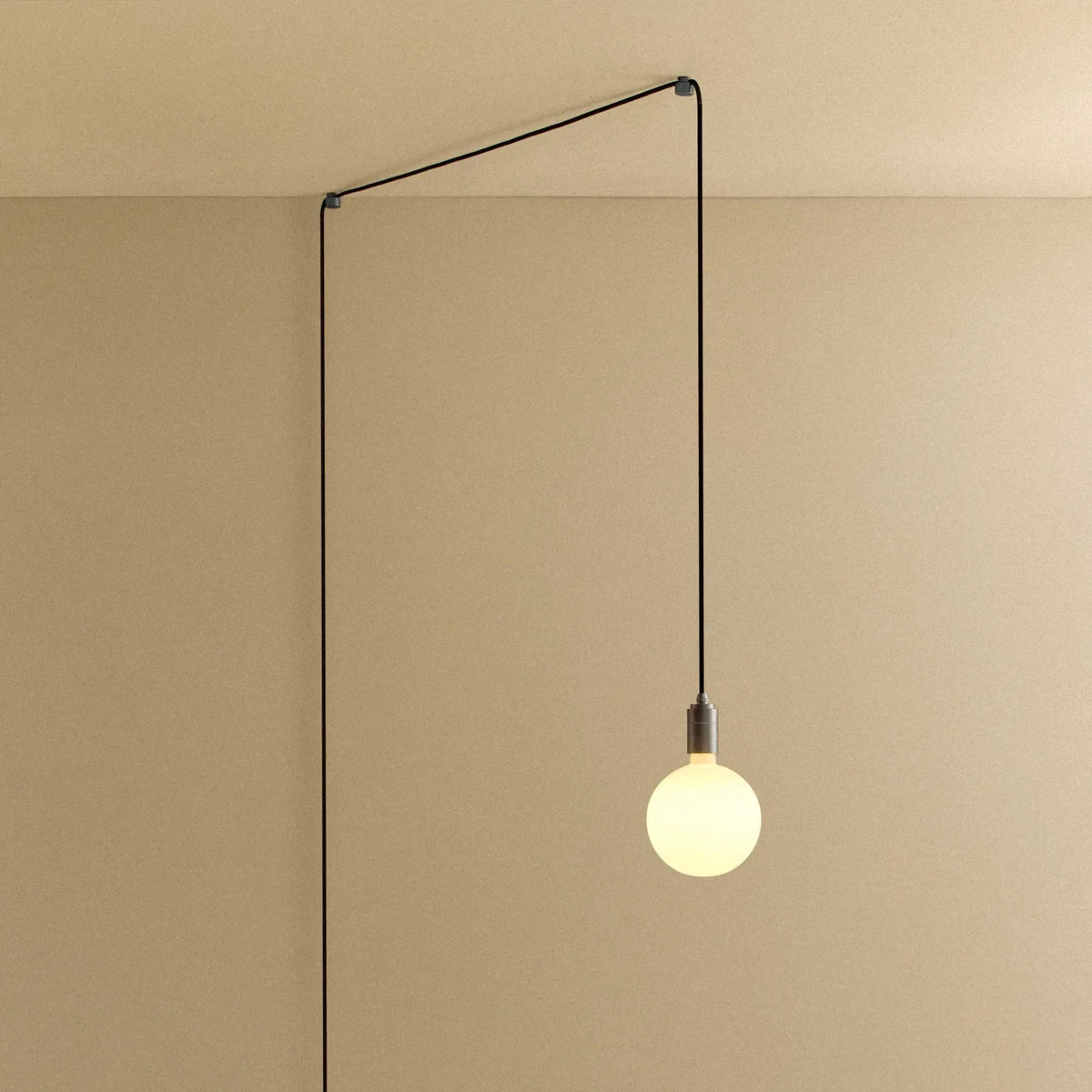 Plug-in pendant with opal globe bulb, graphite, lit, hung from a wall node