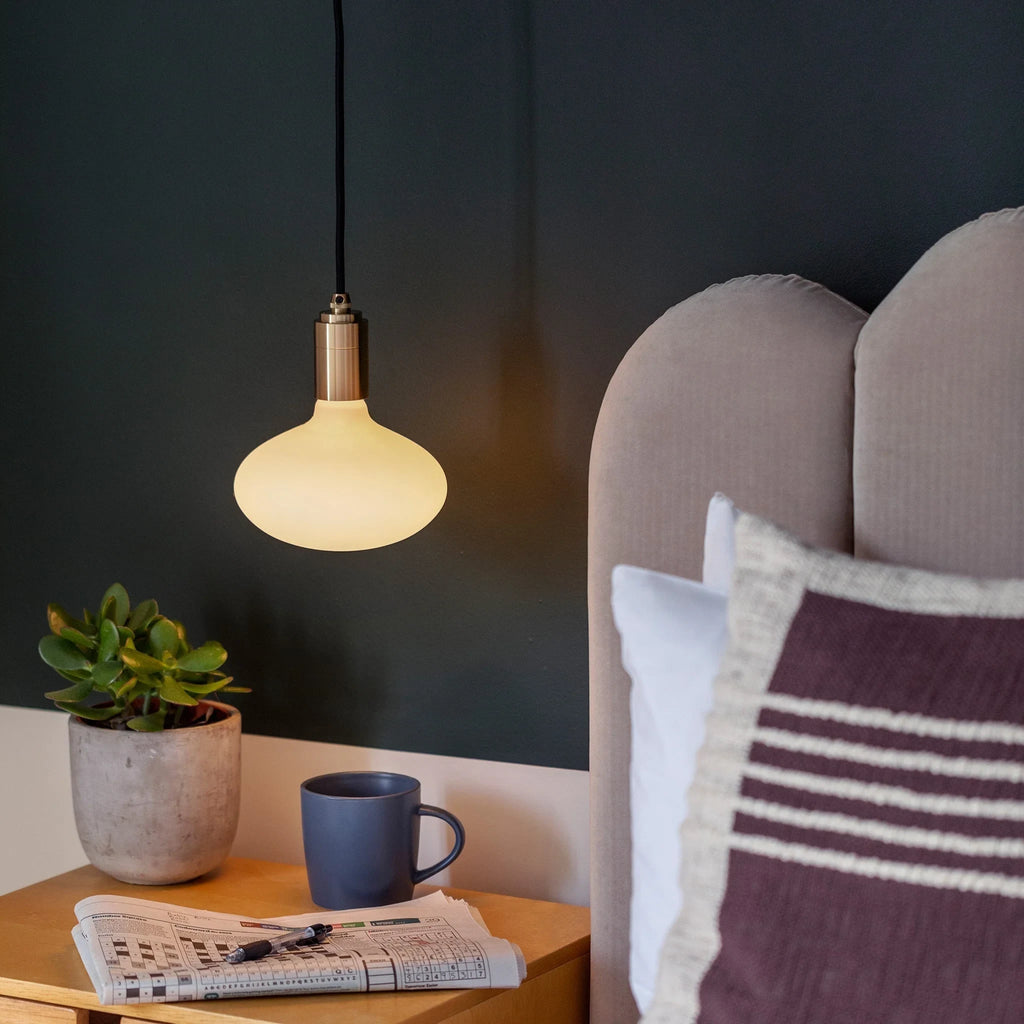 Plug-in pendant with small opal oval bulb, brass, lit beside a bed