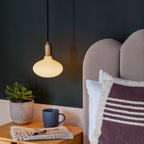 Plug-in pendant with small opal oval bulb, brass, lit beside a bed