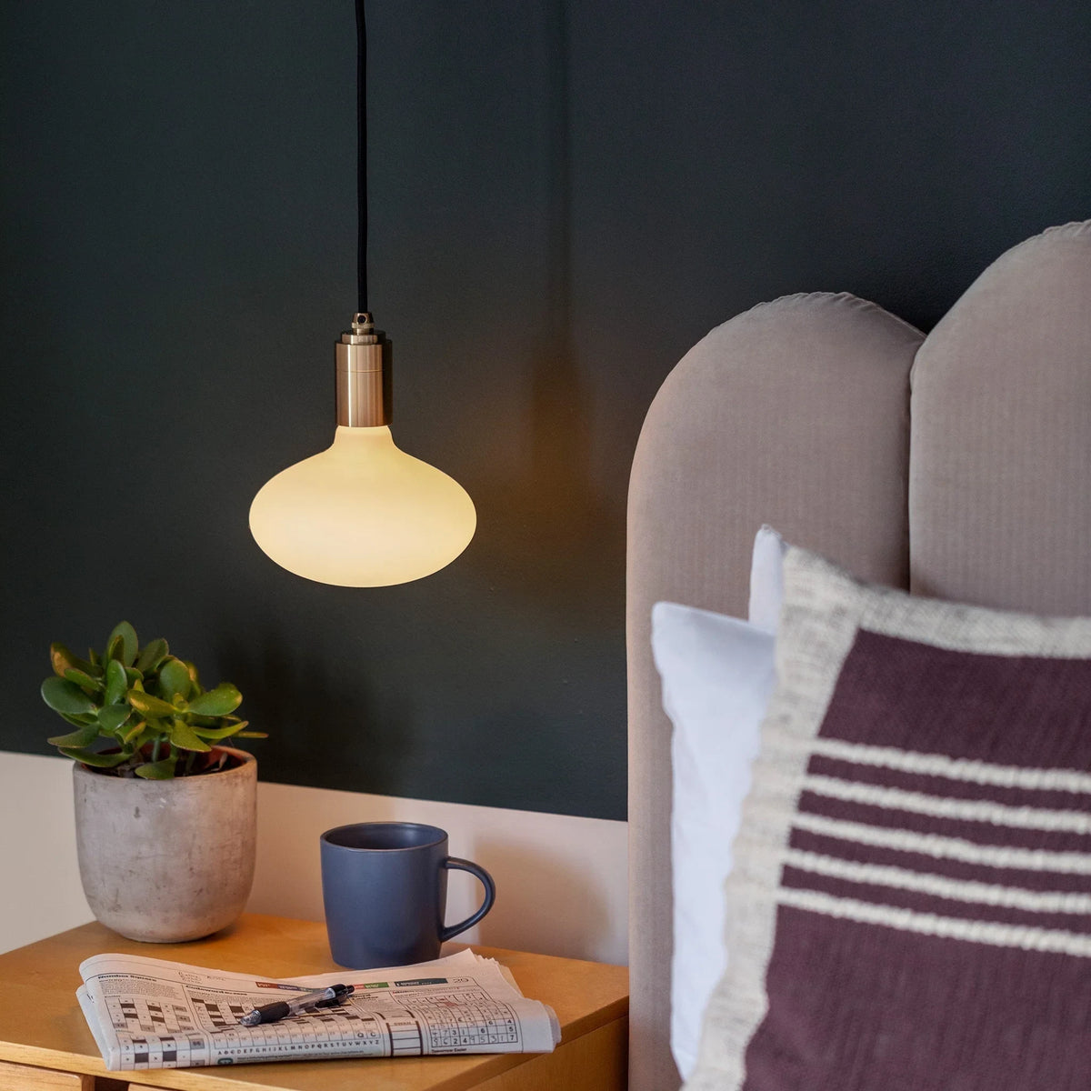 Plug-in pendant with small opal oval bulb, brass, lit beside a bed