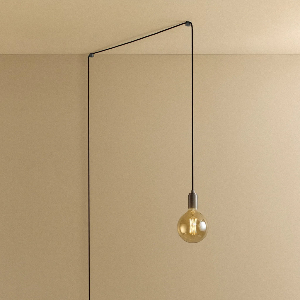 Plug-in pendant with tinted glass globe bulb, graphite, lit, hung from a wall node