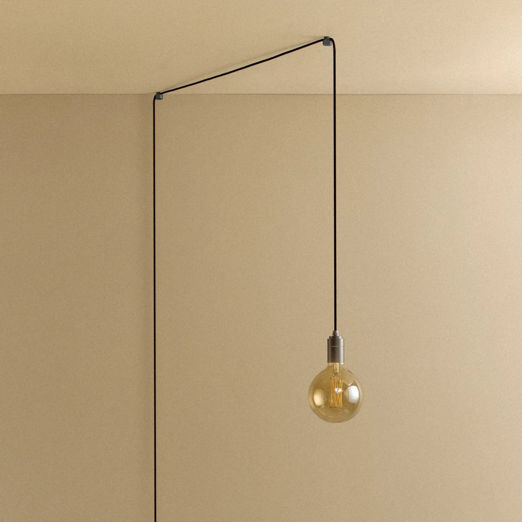 Plug-in pendant with tinted glass globe bulb, graphite, lit, hung from a wall node