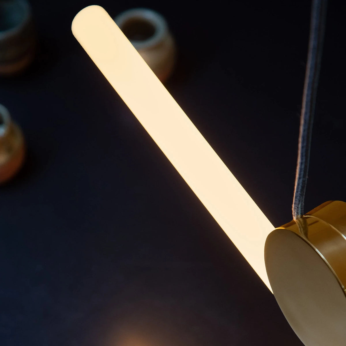 Polished brass linear LED pendant, close-up of the angled tube and brass disc