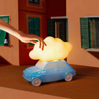 Table lamp with a glowing cloud on a small blue car, lit, with a hand reaching for the cloud