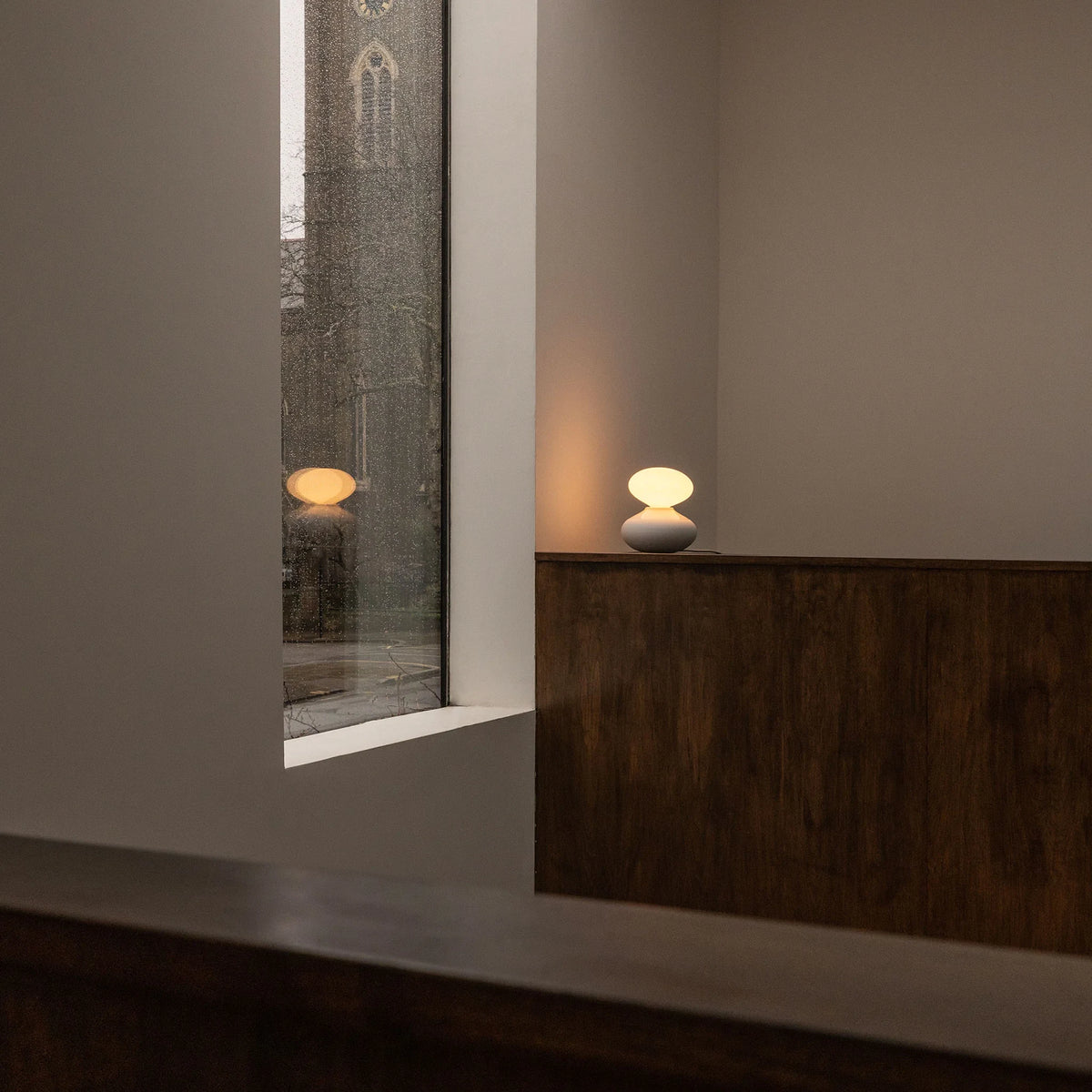 Porcelain oval table lamp, lit on a dark sideboard in a hallway