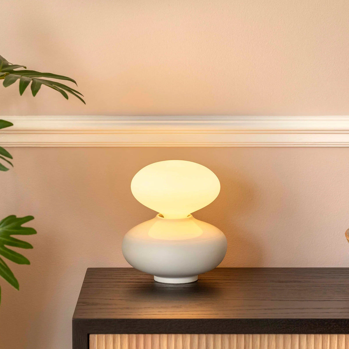 Porcelain oval table lamp, lit on a console beside a plant