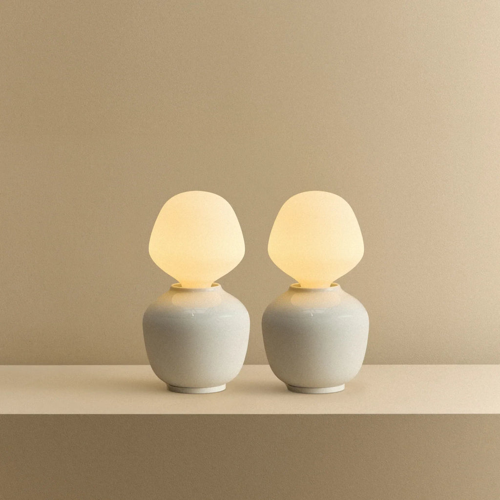 White porcelain table lamp with an angular opal bulb, pair lit, on a shelf