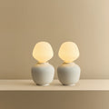 White porcelain table lamp with an angular opal bulb, pair lit, on a shelf