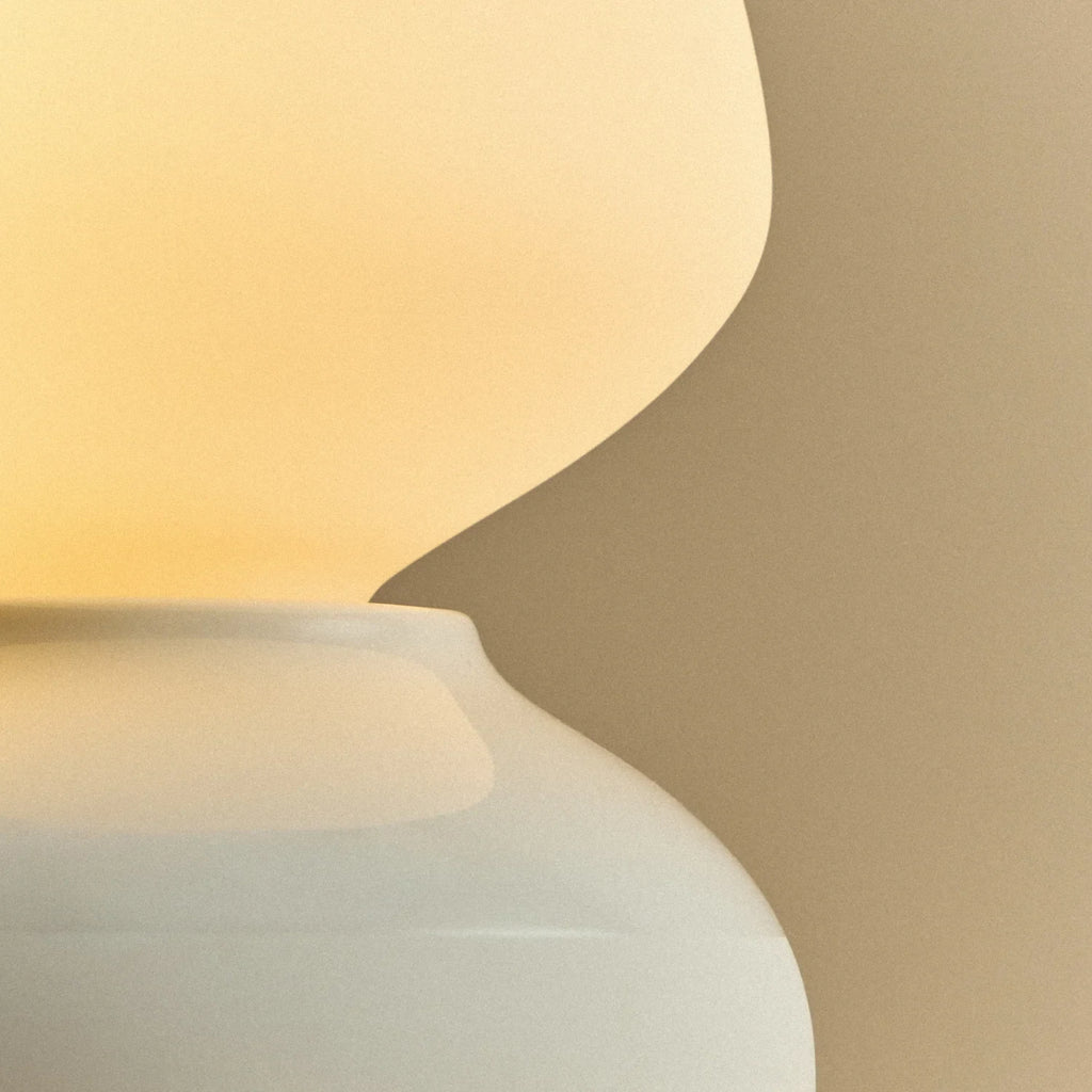 White porcelain table lamp with an angular opal bulb, close-up of the glazed base, lit