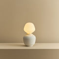 White porcelain table lamp with an angular opal bulb, lit, on a shelf