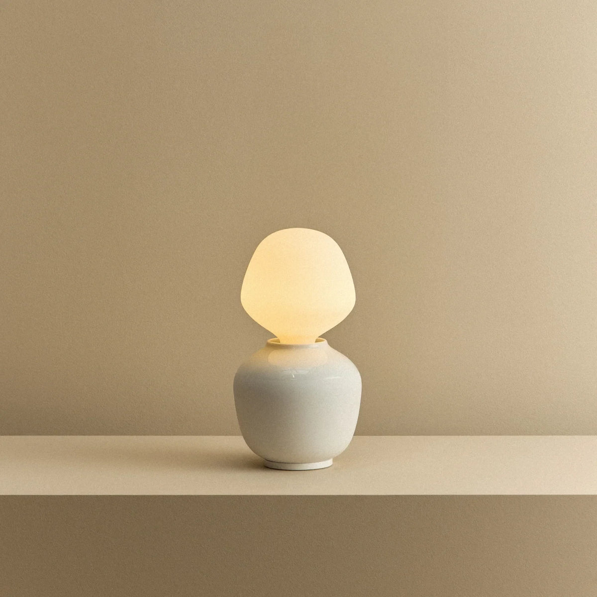 White porcelain table lamp with an angular opal bulb, lit, on a shelf
