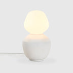 White porcelain table lamp with an angular opal bulb, lit, on a pale background
