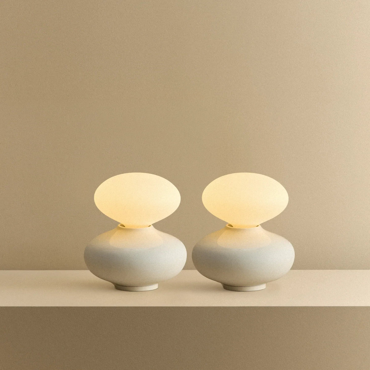 White porcelain table lamp with an oval opal bulb, pair lit, on a shelf