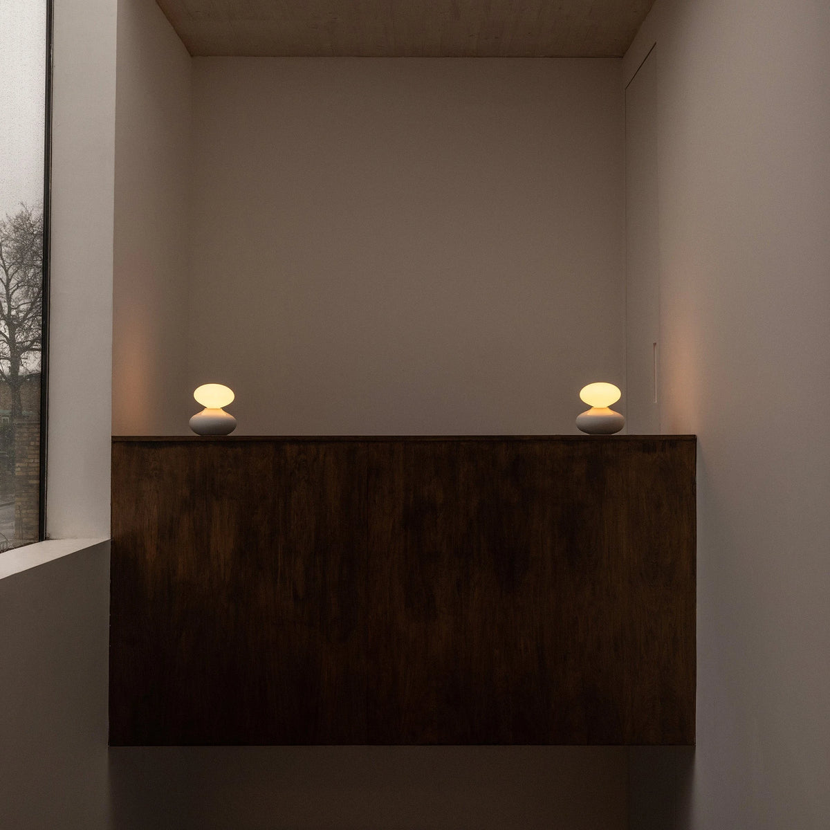 White porcelain table lamp with an oval opal bulb, pair on a dark wooden sideboard in a hallway