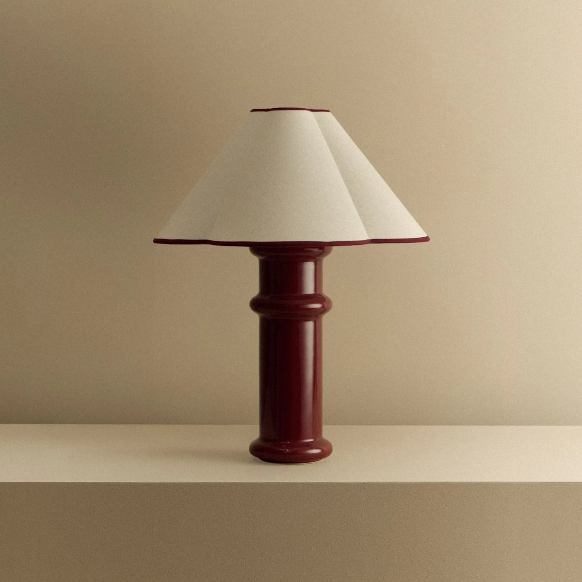 Ceramic table lamp, port red glaze with a folded cotton shade, unlit, on a shelf