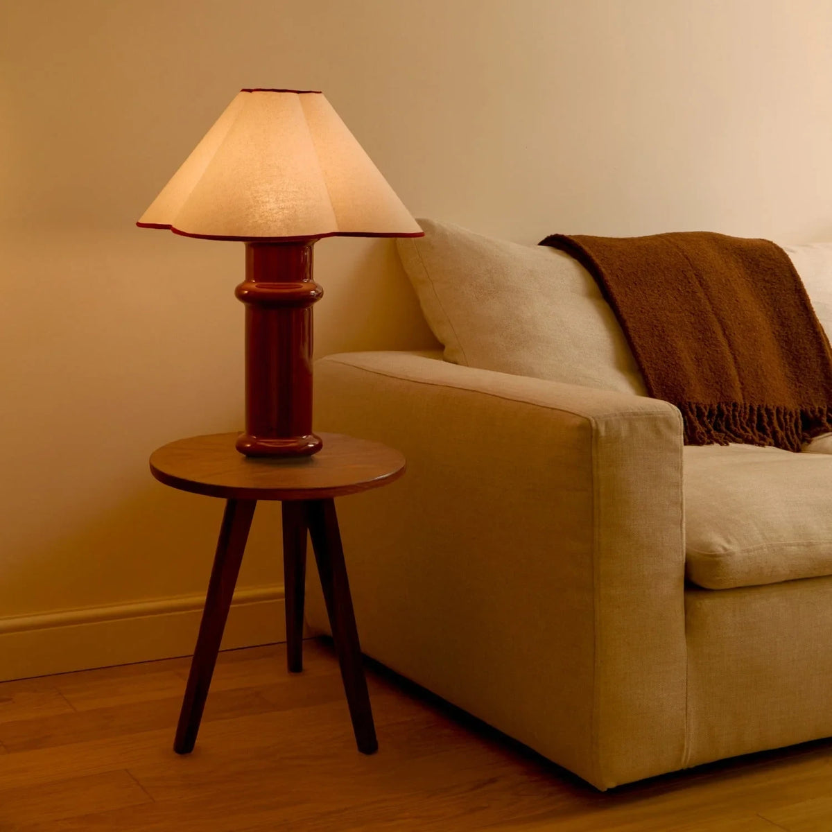 Ceramic table lamp, port red glaze with a folded cotton shade, beside a sofa on a side table