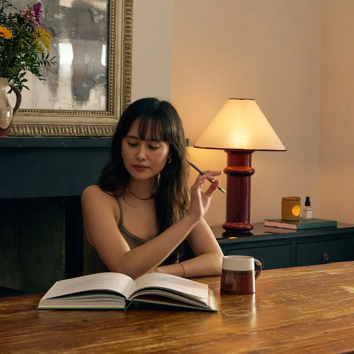 Ceramic table lamp, port red glaze with a folded cotton shade, on a table beside a woman reading