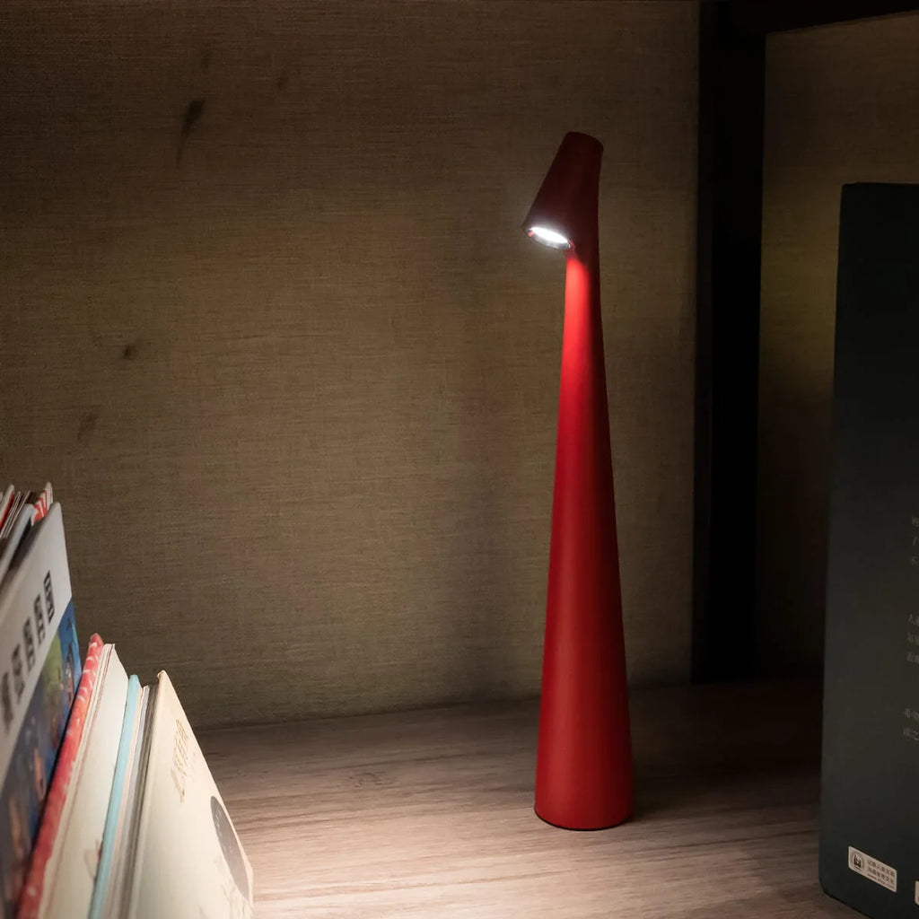 Slim cone cordless table lamp, in red, lit beside books