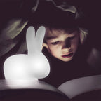 Mini cordless rabbit table lamp, translucent, lit beside a child reading in bed