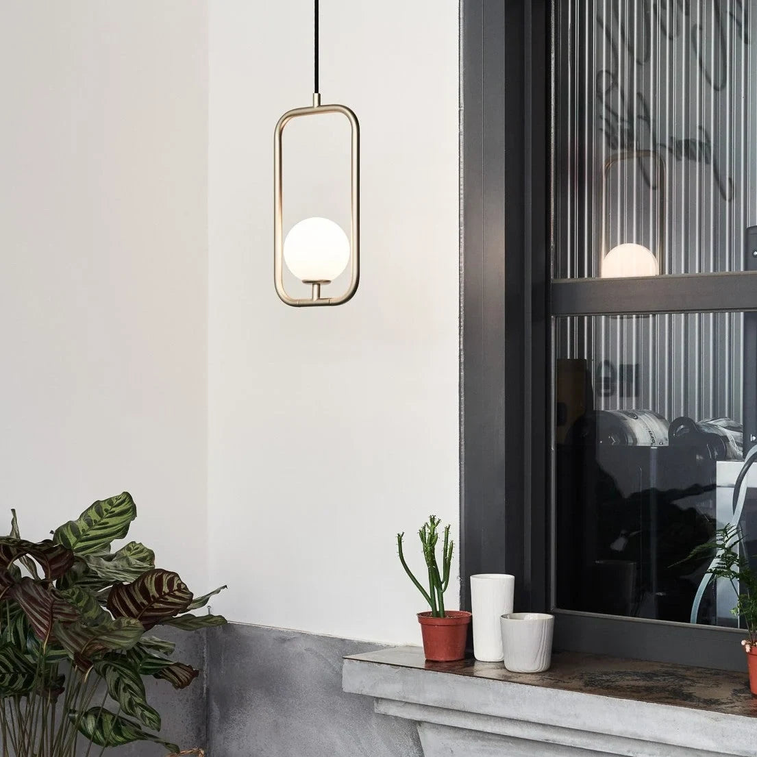 Rectangular Frame Opal Globe Pendant, beside a window with plants
