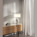 Ribbed sculptural glass table lamp, on a sideboard by a window, with a shade (not included)