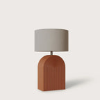 Ridged arch ceramic table lamp, in terracotta with a drum shade, on a plain background