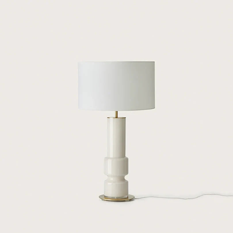 Ridged ceramic cylinder table lamp, in white with a white drum shade, on a plain background
