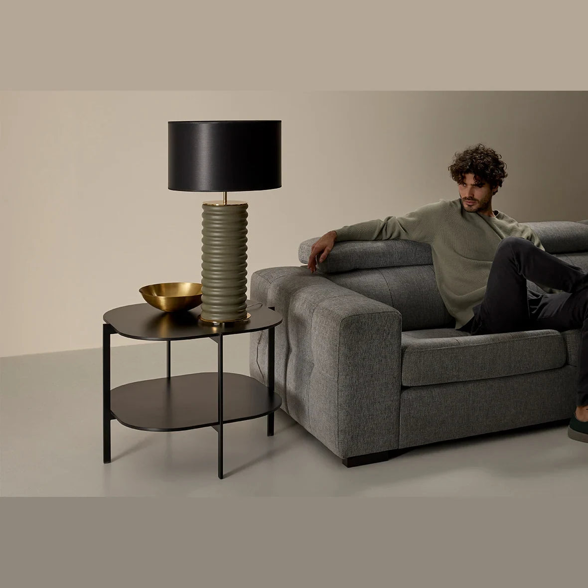 Ridged ceramic cylinder table lamp, in green with a black shade, beside a grey sofa