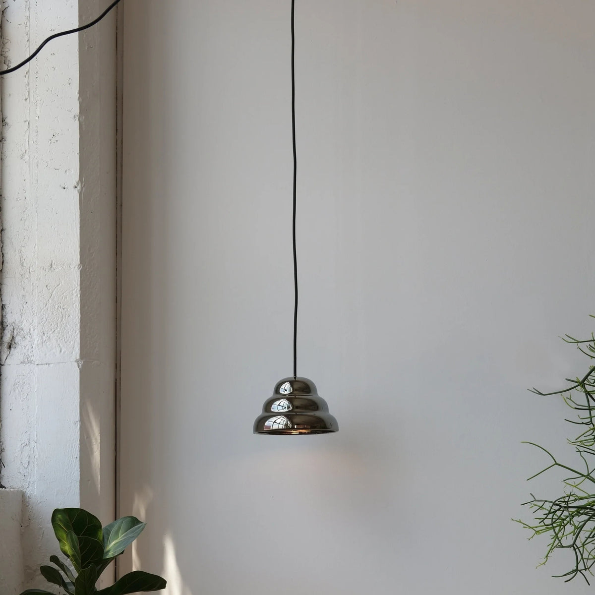Rippled chrome-glaze stoneware pendant, lit in a quiet corner