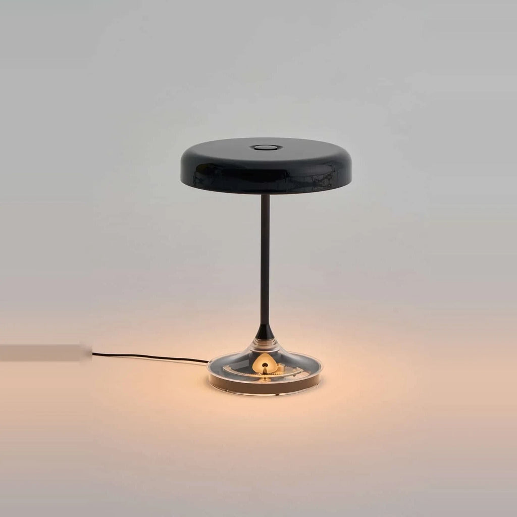 Black disc table lamp with rotating dimmer base, lit, on a plain background