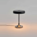 Black disc table lamp with rotating dimmer base, lit, on a plain background