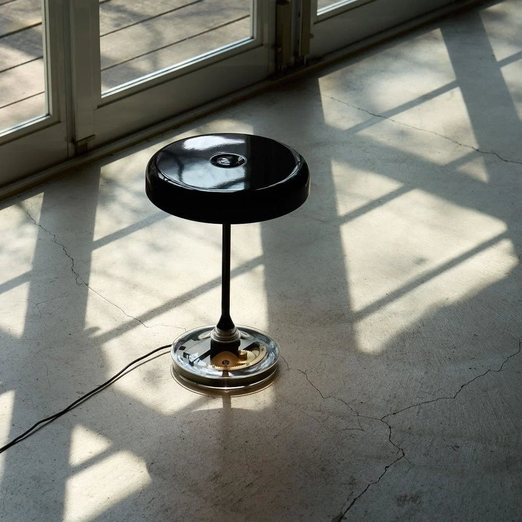 Black disc table lamp with rotating dimmer base, on a sunlit floor