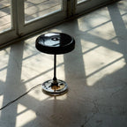Black disc table lamp with rotating dimmer base, on a sunlit floor