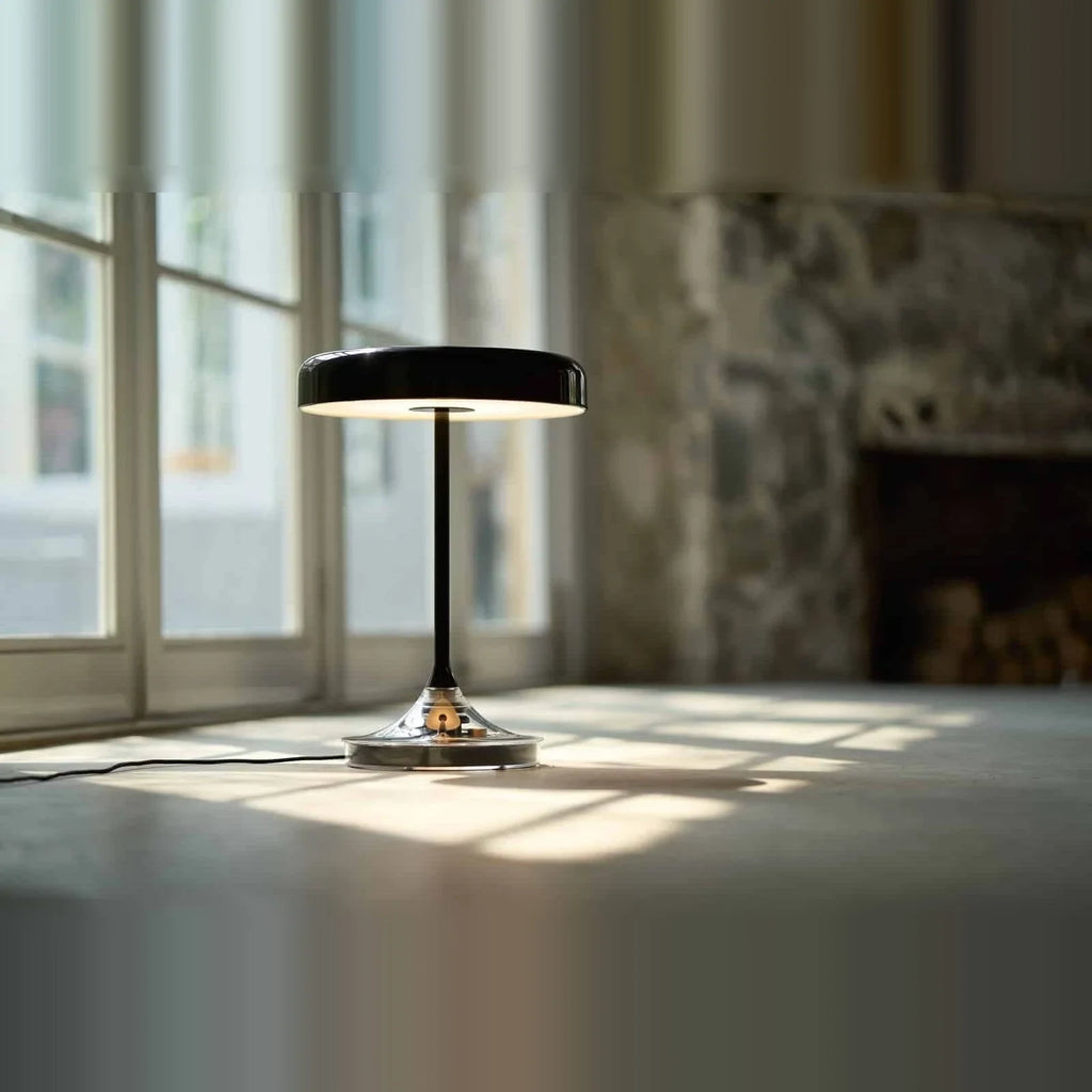 Black disc table lamp with rotating dimmer base, on a floor by a window