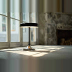 Black disc table lamp with rotating dimmer base, on a floor by a window