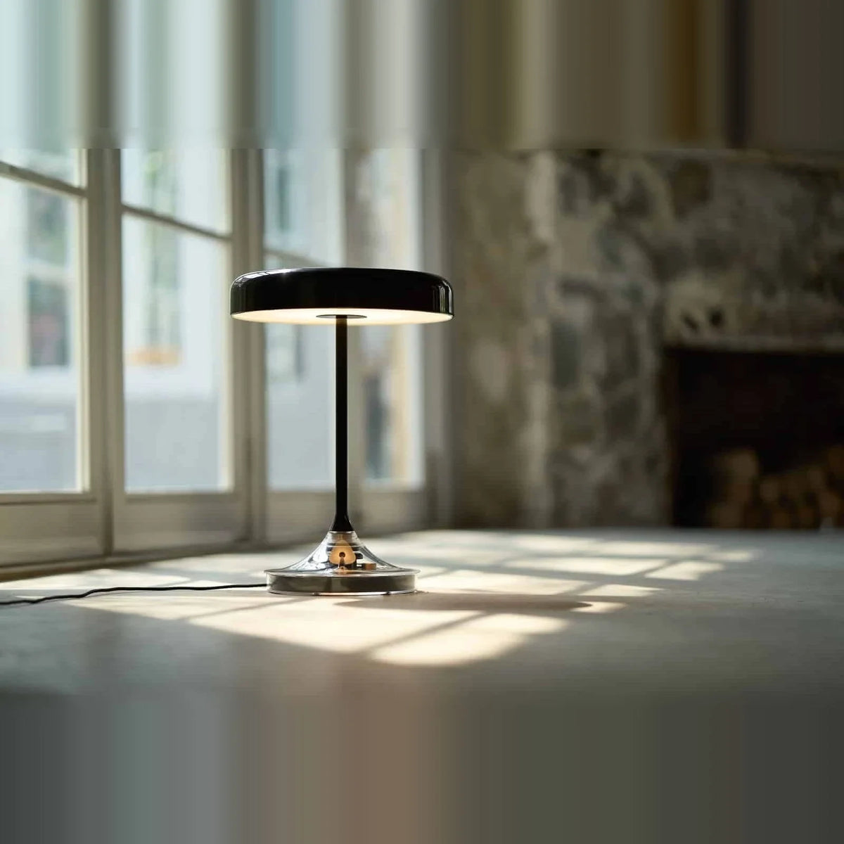 Black disc table lamp with rotating dimmer base, on a floor by a window
