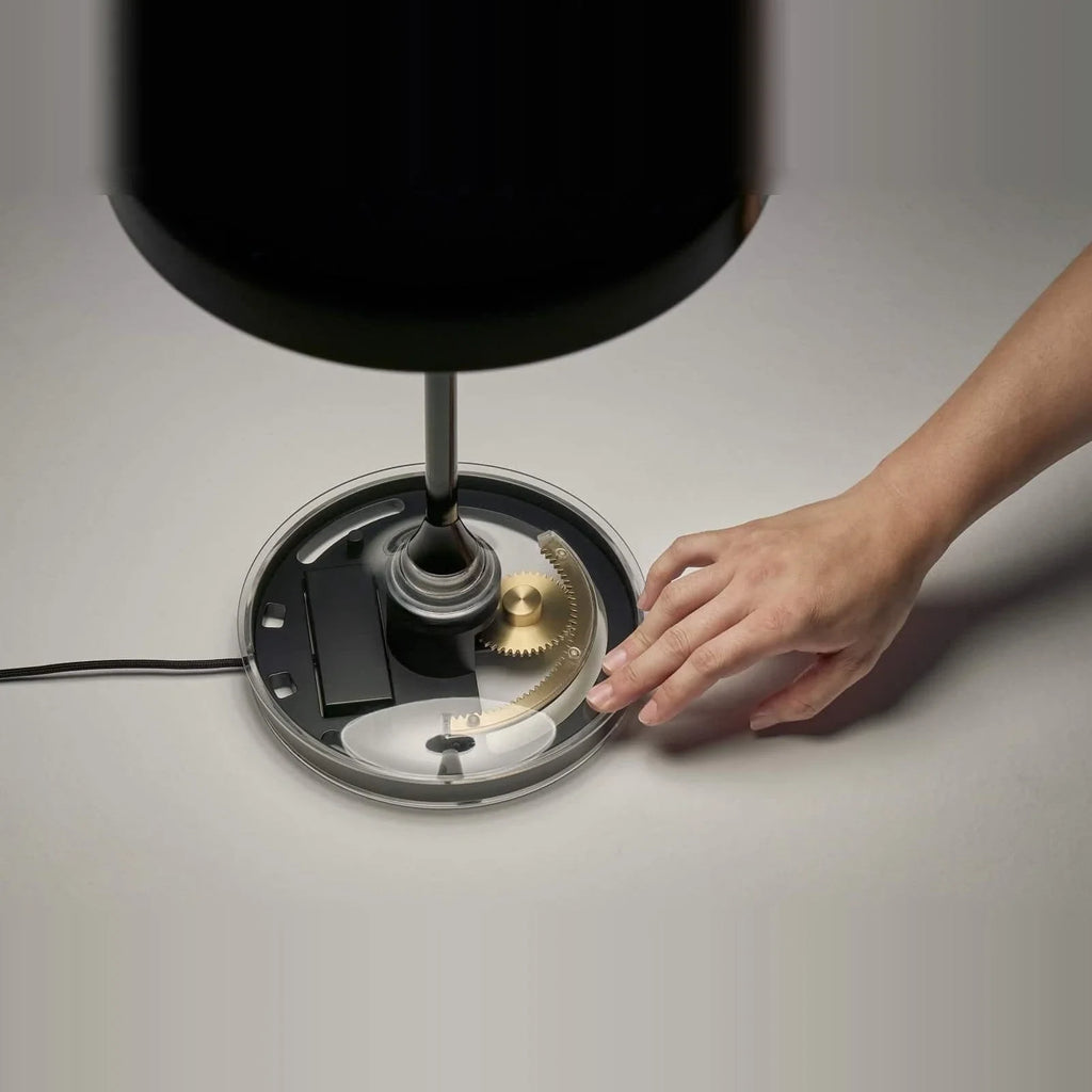 Black disc table lamp with rotating dimmer base, hand turning the base