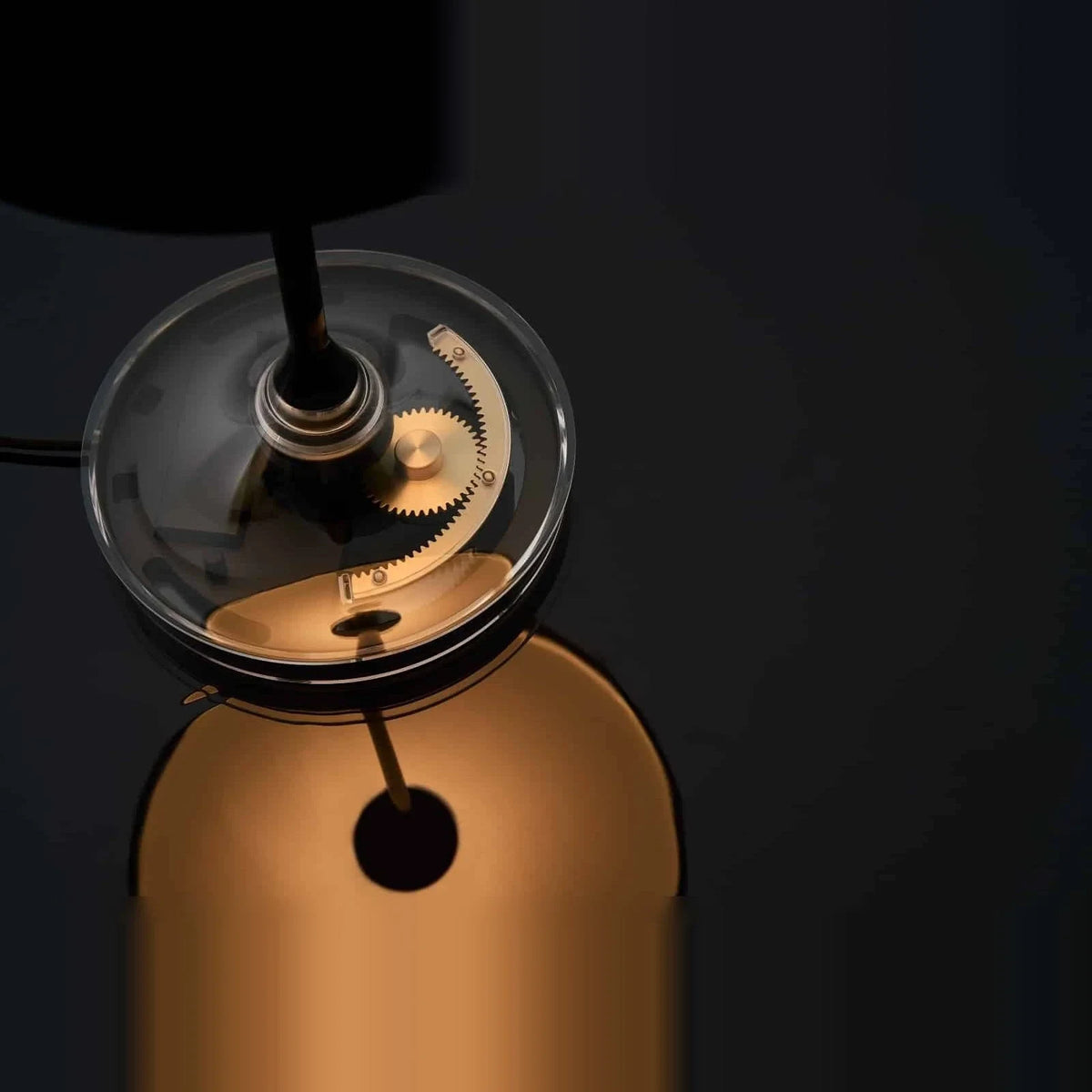 Black disc table lamp with rotating dimmer base, looking down at the gear mechanism