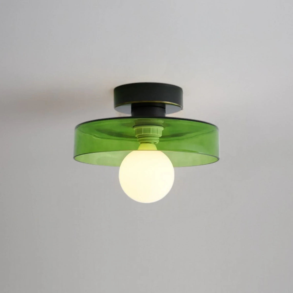 Round glass flush ceiling light, with a black base and green glass, lit