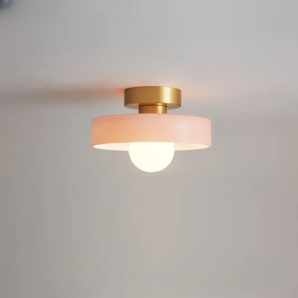 Round glass flush ceiling light, with a gold base and pink glass