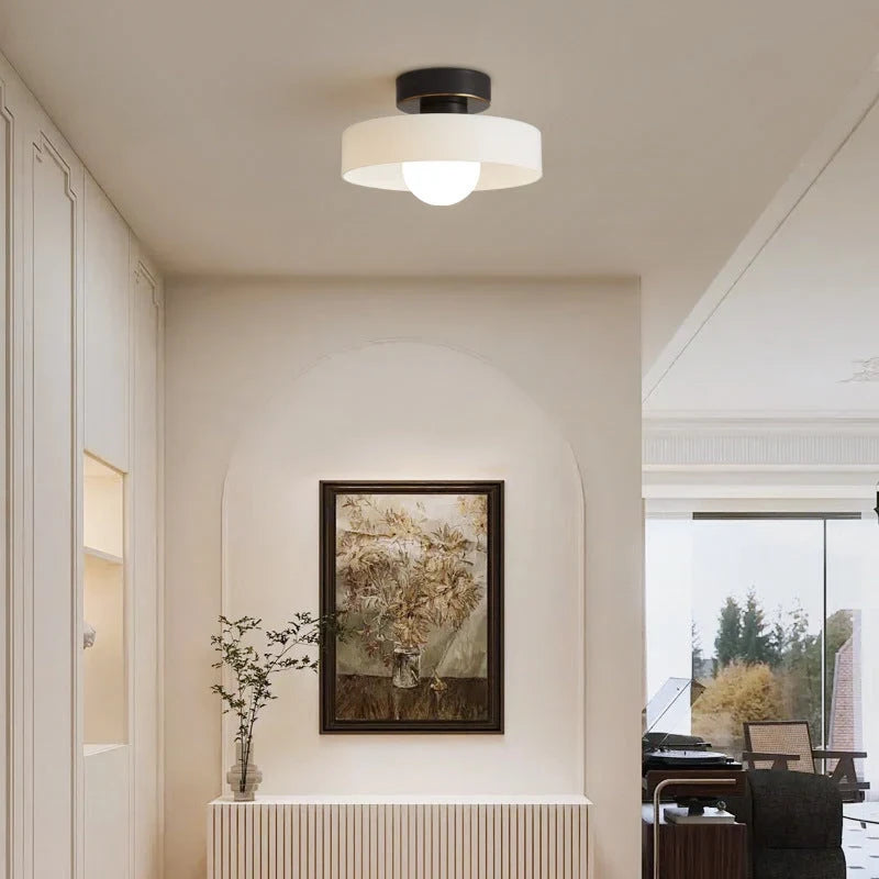 Round glass flush ceiling light, with a black base and white glass in a hallway