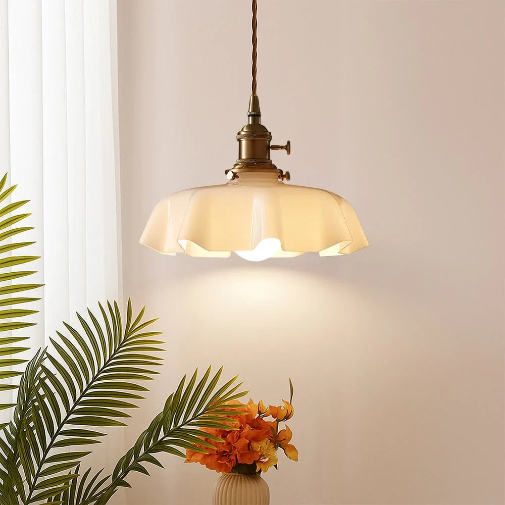Scalloped cream glass pendant light with a brass fitting, lit in a living room