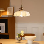 Scalloped cream glass pendant light with a brass fitting, above a dining table