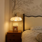 Scalloped cream glass pendant light with a brass fitting, beside a bed