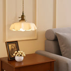 Scalloped cream glass pendant light with a brass fitting, above a side table