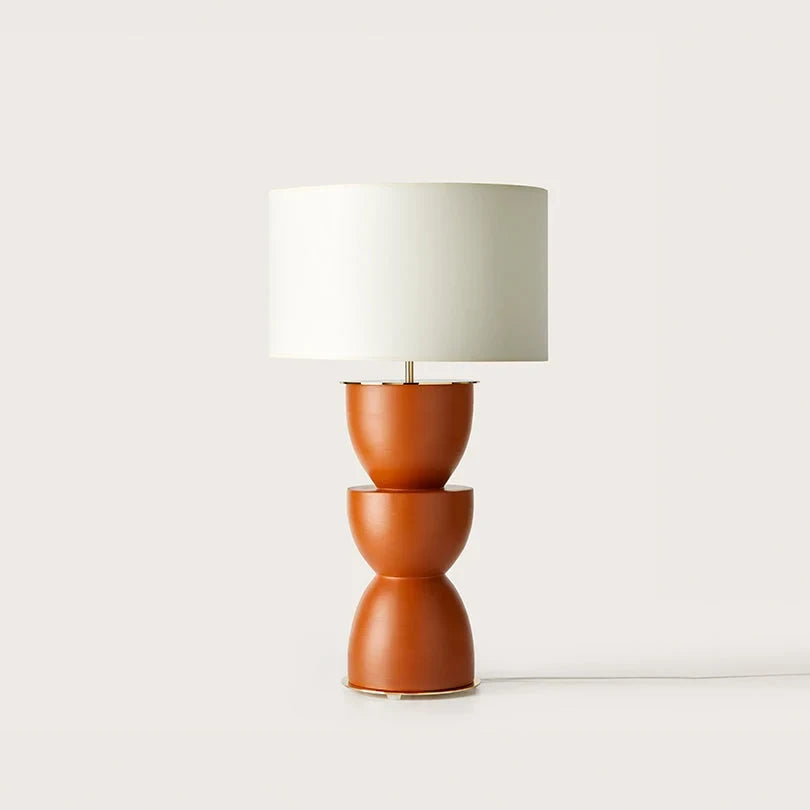 Sculpted stacked ceramic table lamp, in a clay orange with a white drum shade, on a plain background