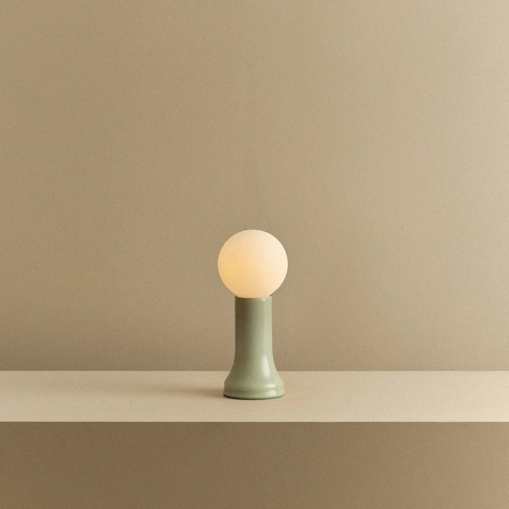 Mouth-blown glass table lamp in sea green, lit, on a shelf