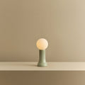 Mouth-blown glass table lamp in sea green, lit, on a shelf
