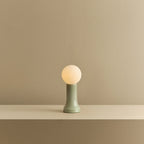 Mouth-blown glass table lamp in sea green, lit, on a shelf