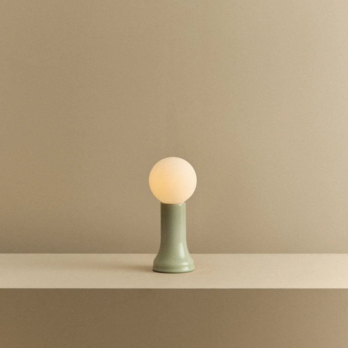 Mouth-blown glass table lamp in sea green, lit, on a shelf